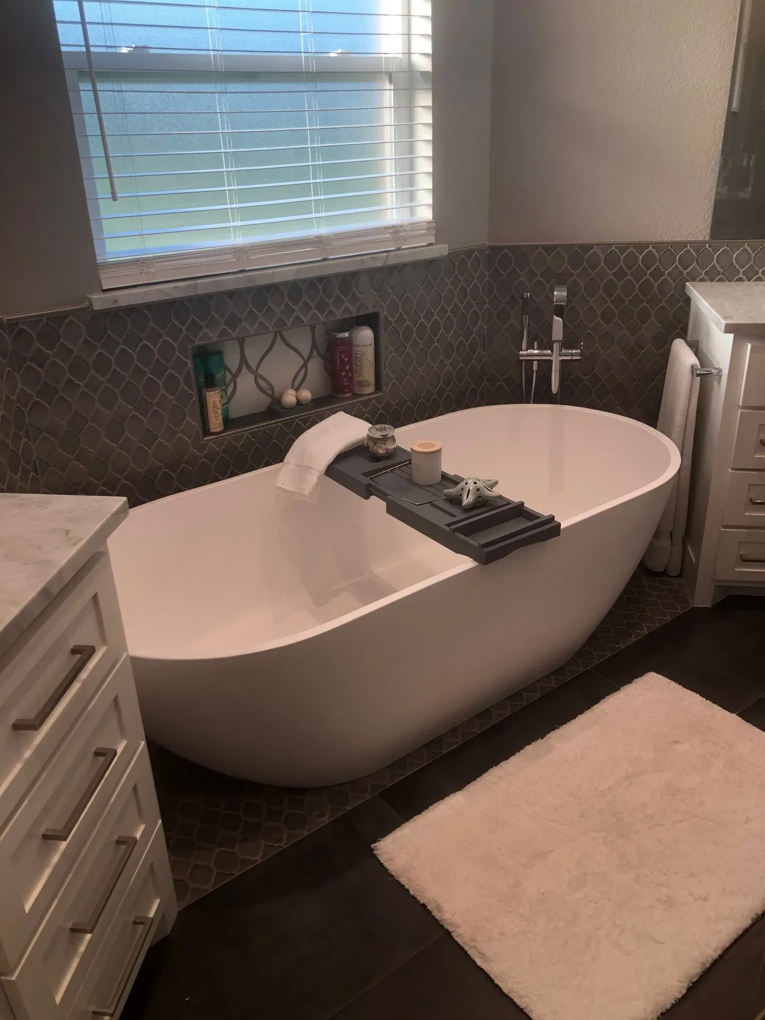 Remodeled bathroom with a freestanding oval tub under a window and dark tile walls