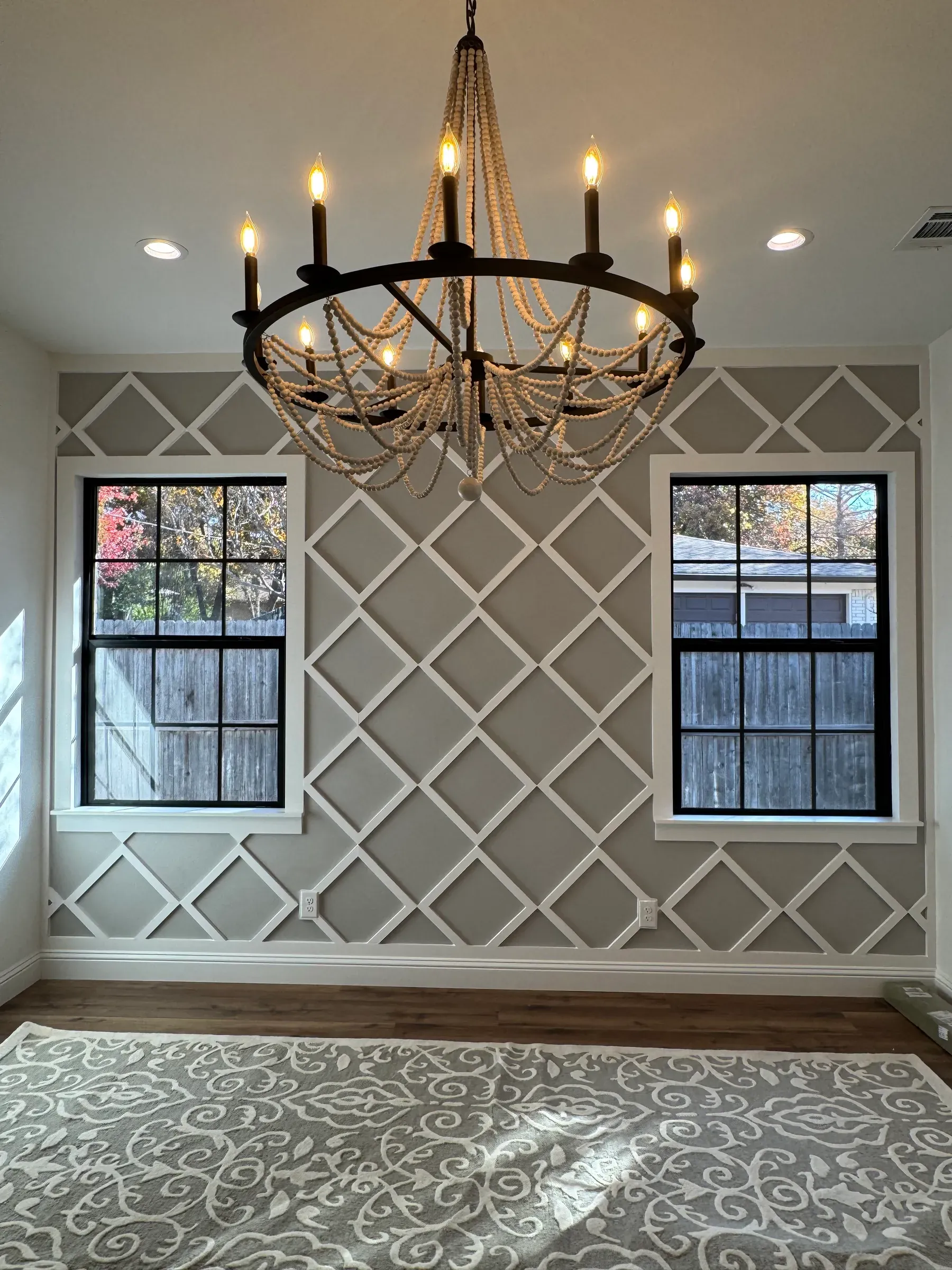 Dining room with a wood bead chandelier, gray trellis wall paneling, and black-framed windows