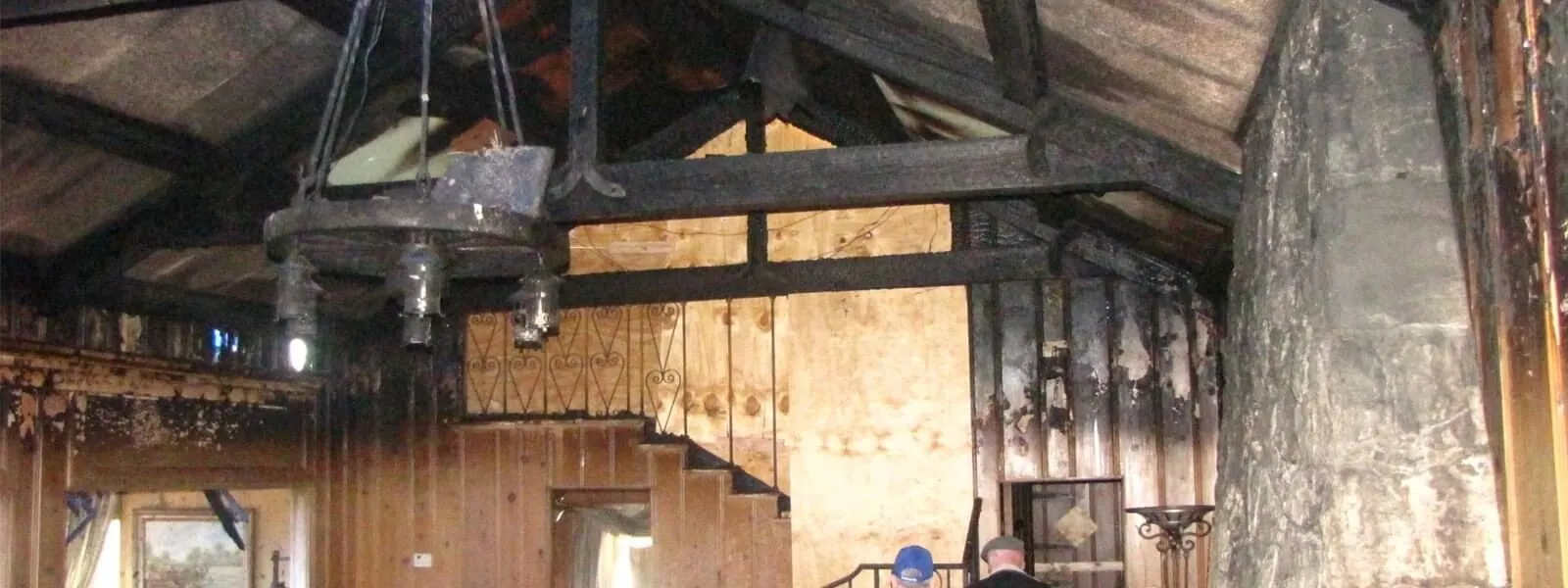Great room after a house fire, with charred ceiling beams and smoke-blackened paneling