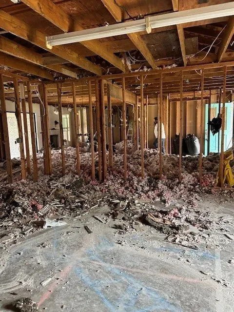 Home interior stripped to the studs and ceiling joists, with insulation and debris on the floor