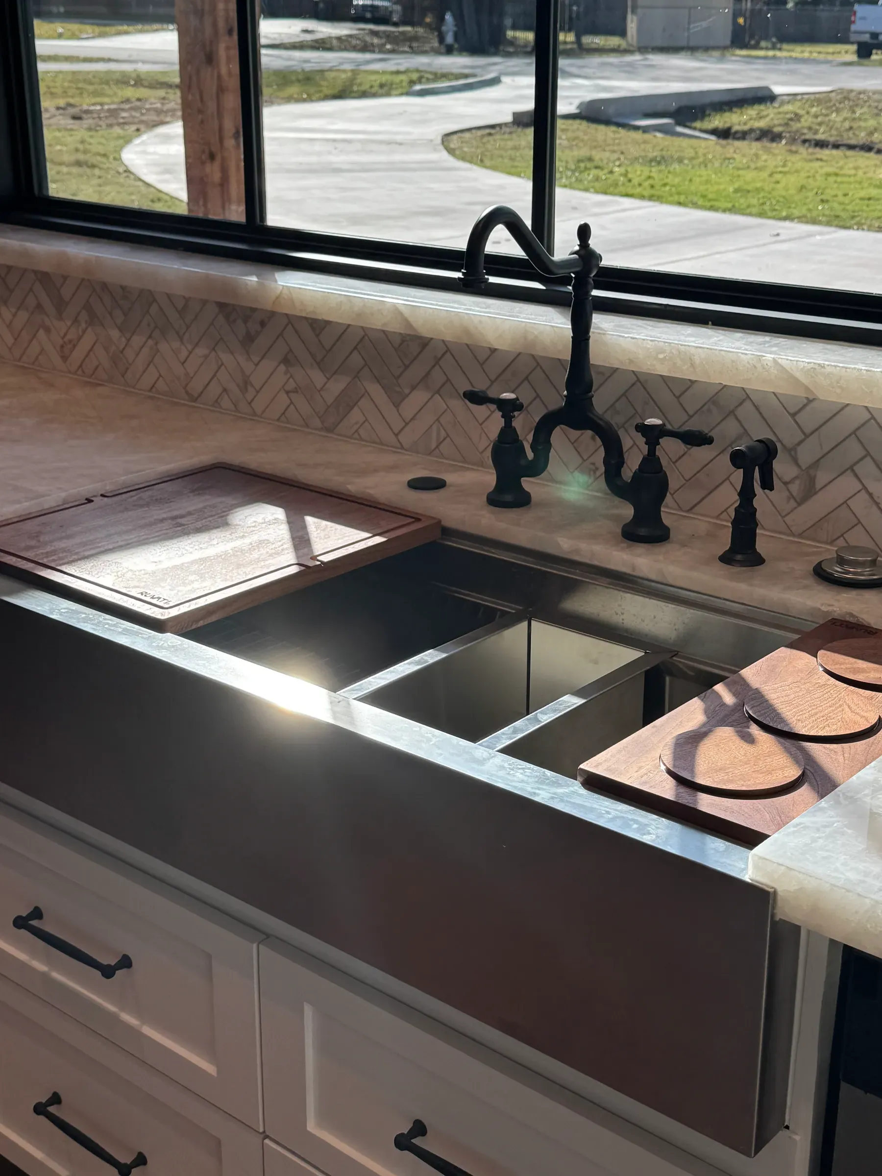 Stainless farmhouse sink with a black bridge faucet under a large kitchen window
