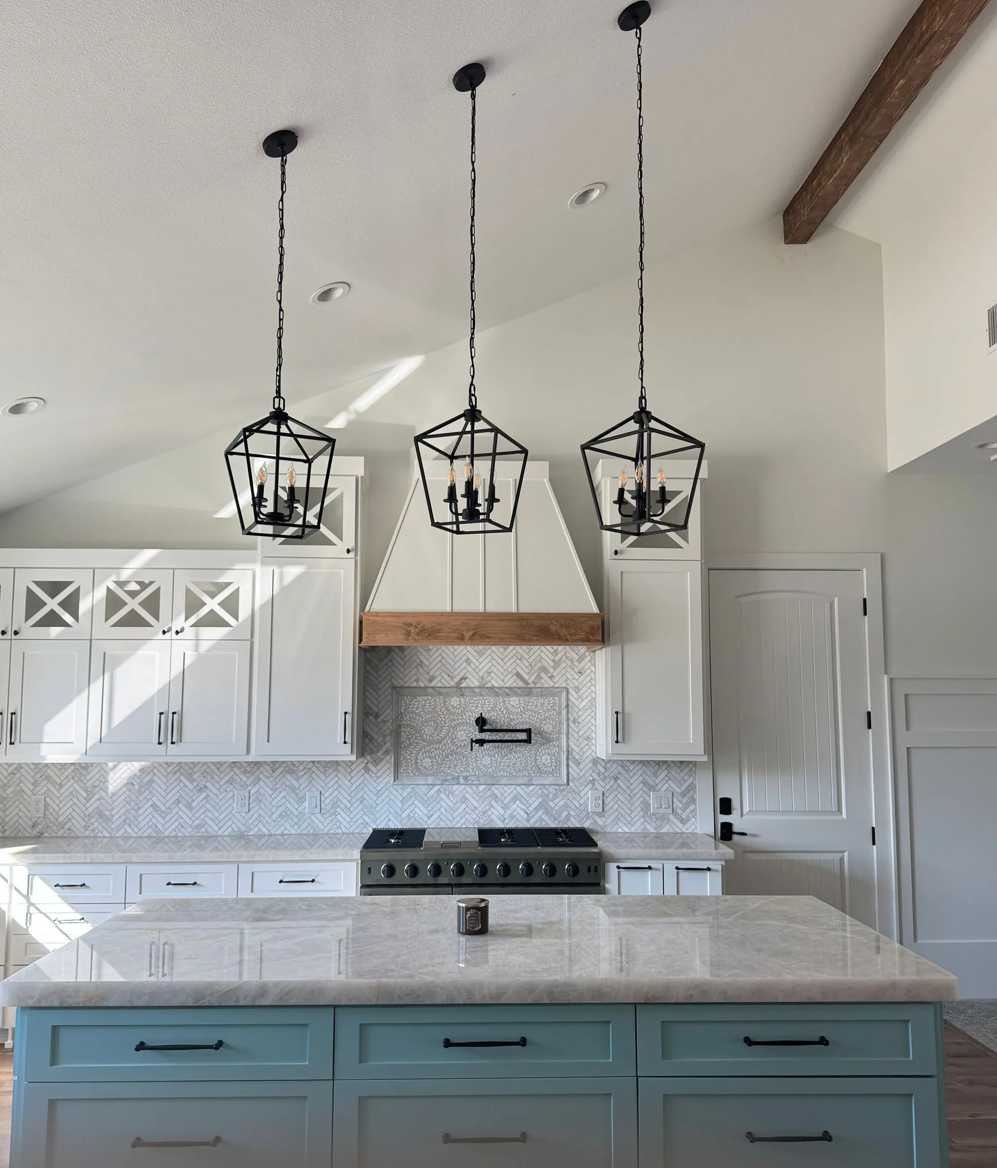 Remodeled kitchen with a blue-green island, marble counters, and three lantern pendants
