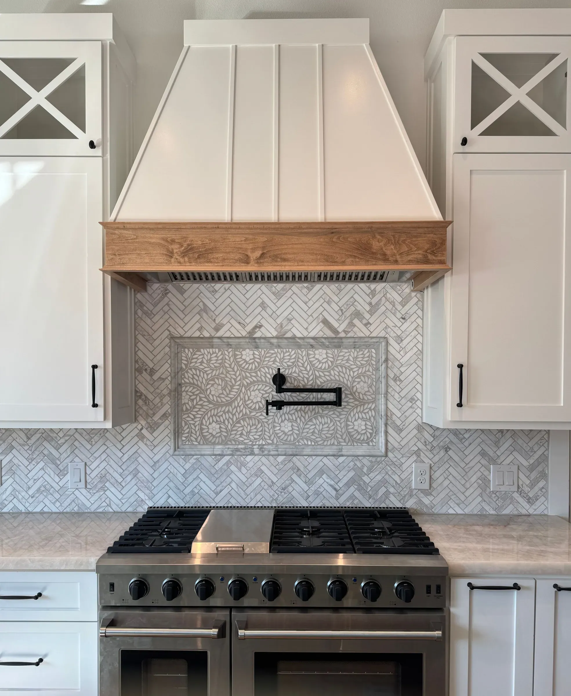 White plaster range hood with a cedar band over a marble herringbone backsplash and gas range